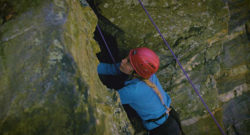 A person wearing safety gear is secured by ropes as they rock climb.